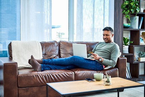 Shot of a man using a laptop and credit card on the sofa at home Shot of a man using a laptop and credit card on the sofa at home